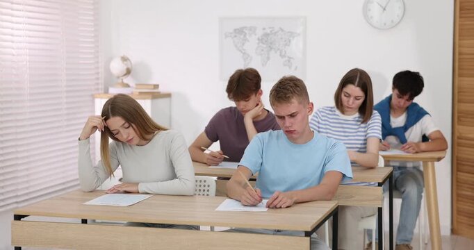 Students taking exam at wooden table indoors