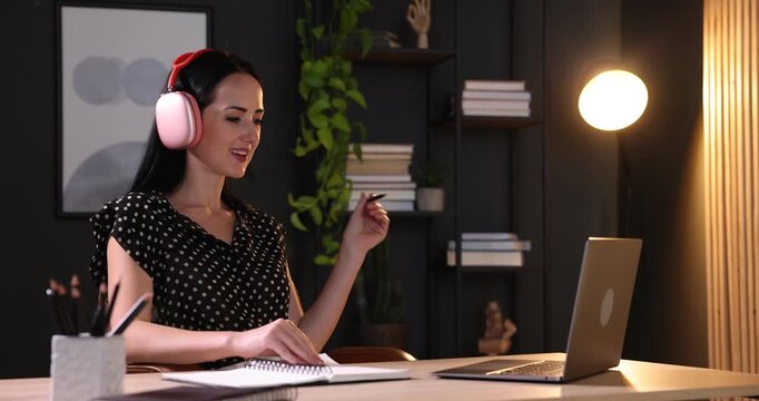 Woman in headphones passing online test via laptop at table indoors