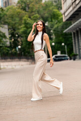Attractive young woman walking confidently on a city street during a warm summer day wearing stylish beige trousers