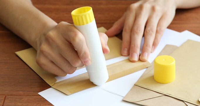 Woman sealing envelope with glue stick at wooden table, closeup