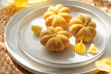 Pumpkin-Shaped Mini Cakes with Cream and Autumn Decor on Woven Placemat