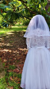 A girl in a white dress and a veil, the image of a scary bride, moves like a zombie on the street, in the park on Halloween