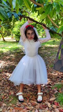 A girl in a white dress and a veil, the image of a scary bride, moves like a zombie on the street, in the park on Halloween