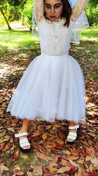 A girl in a white dress and a veil, the image of a scary bride, moves like a zombie on the street, in the park on Halloween