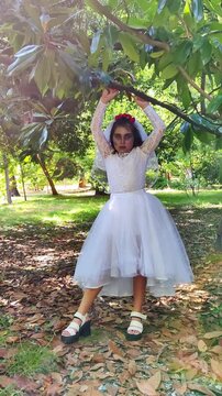 A girl in a white dress and a veil, the image of a scary bride, moves like a zombie on the street, in the park on Halloween