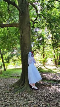 A girl in a white dress and a veil, the image of a scary bride, moves like a zombie on the street, in the park on Halloween