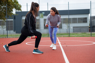 Personal trainer guiding woman during outdoor lunges with dumbbell