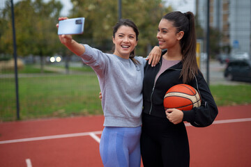 Women friends taking selfie with smartphone on basketball court
