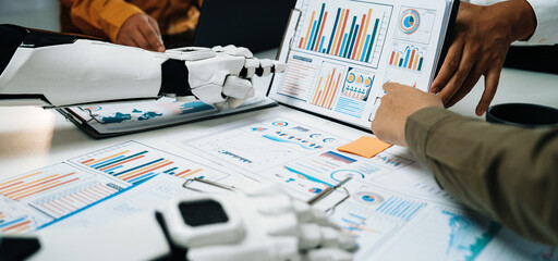 Human and robotic hands engage in a collaborative analysis of business data, showcasing graphs and charts in a modern office setting, emphasizing innovation and teamwork.Noogenesis