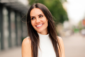 Charming adult woman with a vibrant smile enjoying a stroll in an urban city setting, exuding...