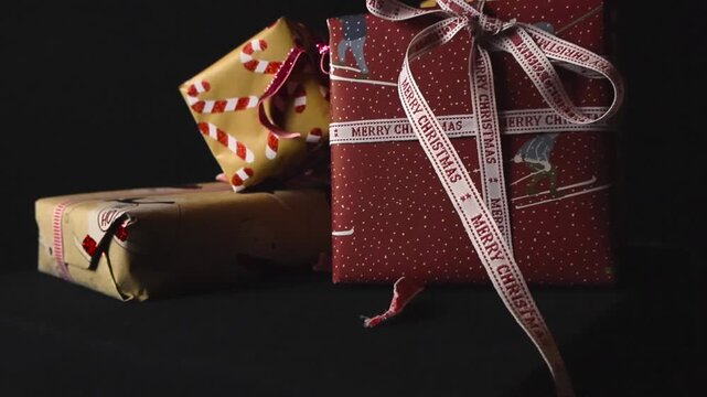 Close up view of colorful and beautiful Christmas presents or holiday gifts with ribbons that say Merry christmas in front of black studi background. Shallow depth of field, bokeh.