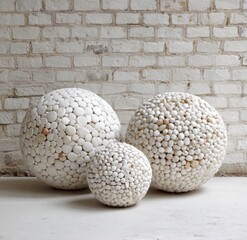 Three spherical decorative objects, composed of numerous small, white stones, are displayed against a white brick wall.