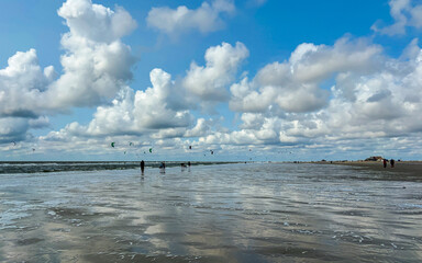 Sea coast after low tide, blue sky clouds reflected in low tide water, numerous flyboards