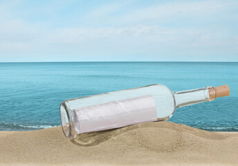 Corked bottle with rolled letter inside on sand near sea
