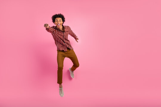 Young man in stylish casual wear jumping enthusiastically against vibrant pink background in joyful attitude