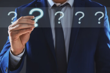 Businessman touching question mark on virtual screen against dark background, closeup