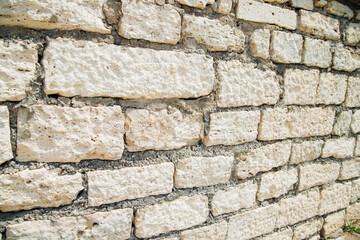 Textured wall of rectangular stone blocks in light beige shades and cement between them.
