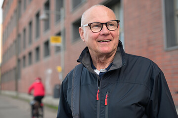 Portrait of a smiling senior man with eyeglasses waiting at a bus stop in the city