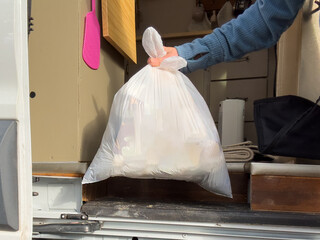Closeup of a person holding a white trash bag full of garbage