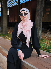 Portrait of a young fashionable Muslim woman in hijab sitting at the city bench.