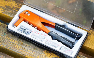 Tool kit with an orange hand riveter and fasteners on a wooden surface in daylight