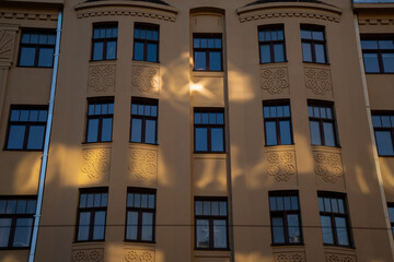 Evening sunlight reflecting off urban building facade with repeating windows and soft shadows, creating geometric harmony, texture and a warm architectural atmosphere of timeless urban design style