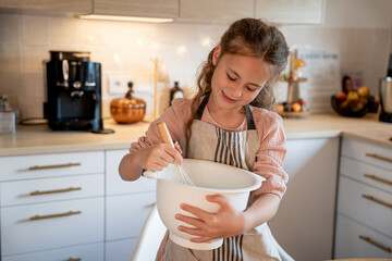 Little cute girl is beating eggs in the kitchen. Homemade baking. Cozy autumn.