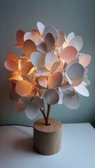 A decorative, illuminated table lamp with a cluster of delicate, paper leaves in soft pinks and whites, casting a warm glow.