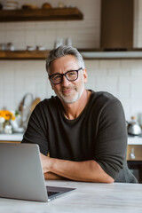 Silver-haired man smiles in kitchen setting while working from home on laptop, creating a sense of focus and balance.