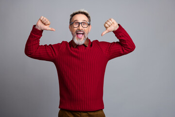 Fototapeta premium Cheerful businessman in casual red pullover pointing at himself and expressing happiness while posing against a solid background
