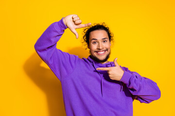 Young man in purple hoodie poses against yellow background with a cheerful expression, gesturing positively and confidently