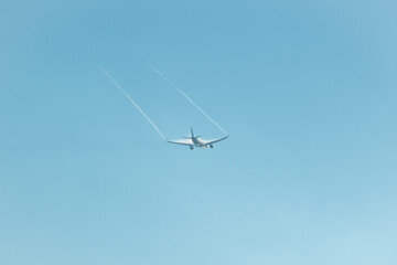 A passenger plane moves away into the blue sky. Flow separation, wingtip vortices are visible at the tips of its wings, creating contrails.