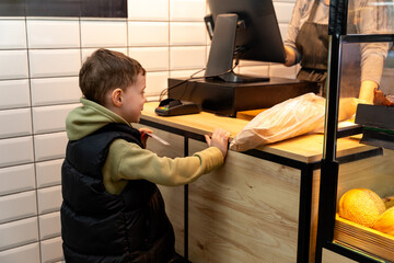 Cute child little boy choosing baked goods or pastry in bakery shop. Little boy buying bread or buns at grocery supermarket and paying by credit card. High quality photo