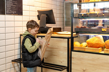 Cute child little boy choosing baked goods or pastry in bakery shop. Little boy buying bread or buns at grocery supermarket and paying by credit card. High quality photo