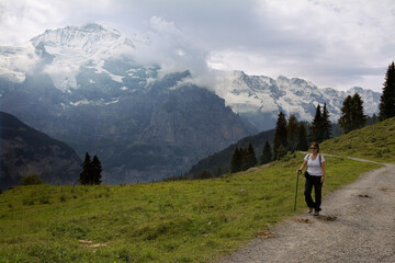 The spectacular Jungfrau massif and the Lauterbrunnen valley from an alp near Grütschalp with a solo female hiker in the foreground, Bernese Oberland, Switzerland