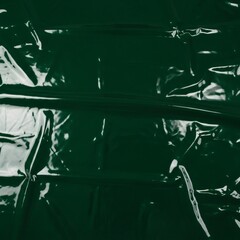 Glossy green latex fabric background with smooth, reflective texture and subtle folds. The surface gleams under light, creating a vibrant, futuristic, and high-contrast visual. Ideal for fashion