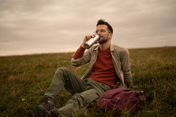 Hiker drinking water resting on grassy field during trek