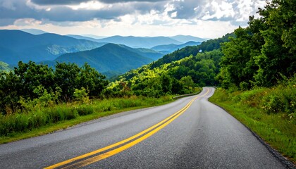 A winding road snakes through verdant mountains under a cloudy sky. The road stretches towards the horizon. Lush trees and foliage flank the path
