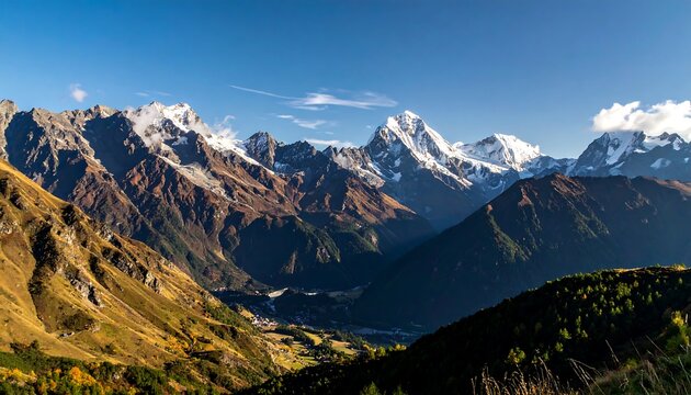 A wide shot of a mountain range with snow-capped peaks, golden and green lower slopes, and a clear blue sky