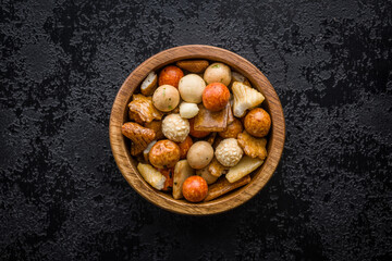 Salted snack. Coated peanuts and mini crackers in bowl on black table.