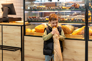 Little boy eating a freshly baked baguette bought from a bakery. High quality photo. Bread and breakfast concept,
