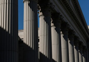 Obraz premium Majestic architectural greek columns detail against blue sky with deep shadows, symbolic for justice, law, power, or historical institution.