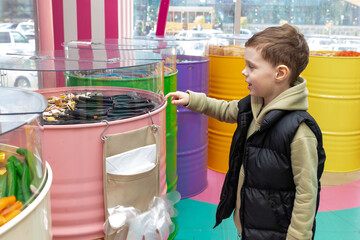 A little boy chooses gummies at a candy store. Unhealthy food for kids. Unhealthy snack. High quality photo