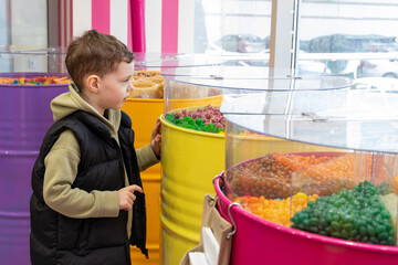 A little boy chooses gummies at a candy store. Unhealthy food for kids. Unhealthy snack. High quality photo