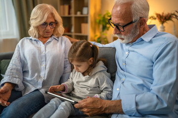 Obraz premium Grandchild using digital tablet with her grandparents at home
