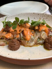 Italian Crudo with Orange Sauce, Olive Tapenade and Microgreens; crudo dish featuring thin slices of raw fish topped with creamy orange sauce, olive tapenade, and fresh microgreens
