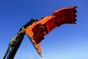 Modern crane arm with open grapple, industrial gripper on blue sky background