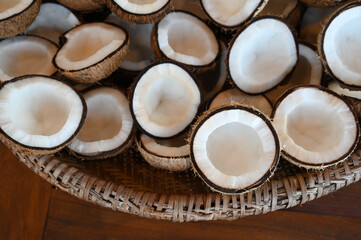 overhead close-up shot of many half-cut Cocos nucifera fruits in a woven basket, fresh natural coconut meat texture and pattern background, healthy tropical food ingredient for oil or water
