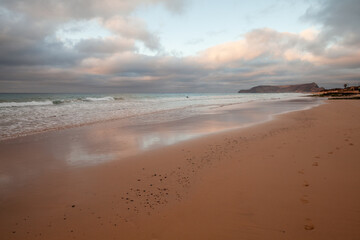 A tranquil seascape featuring soft pink and orange skies, gentle waves