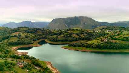 Countryside view of lake farmland and mountain slopes under cloudy sky © Viola